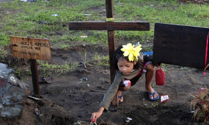 24h qua ảnh: Bé gái cắm kẹo mút lên mộ 4 người thân